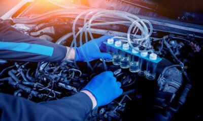 A man in blue gloves holds a bottle of oil, demonstrating how to improve fuel efficiency with a new diesel injector.