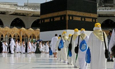 People in white robes and hats standing around the Kaaba during Umrah trip