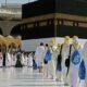 People in white robes and hats standing around the Kaaba during Umrah trip