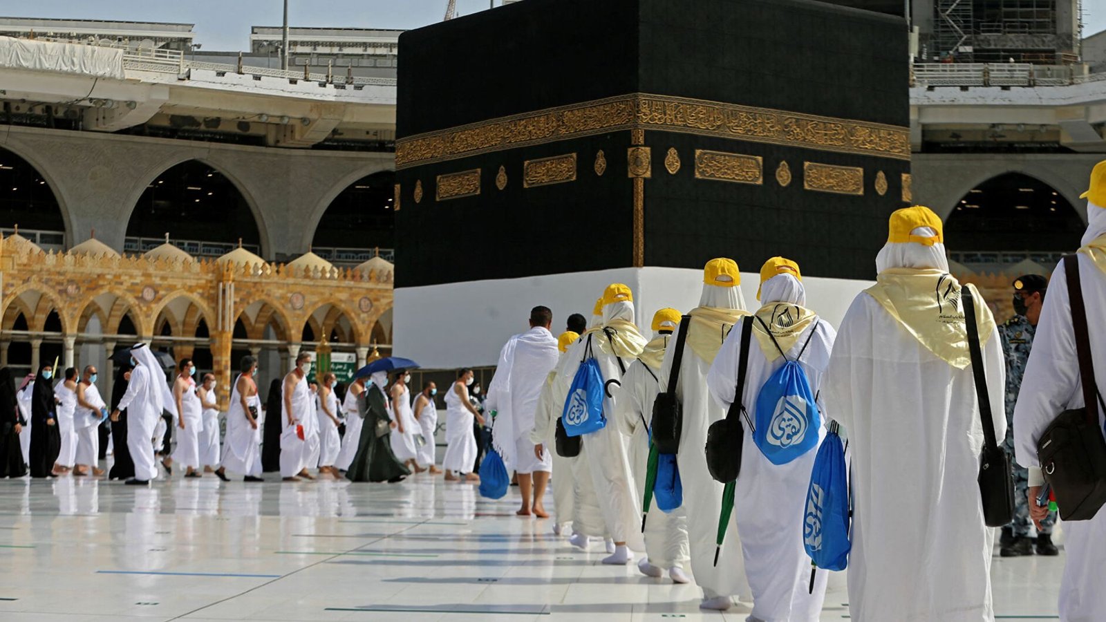 People in white robes and hats standing around the Kaaba during Umrah trip